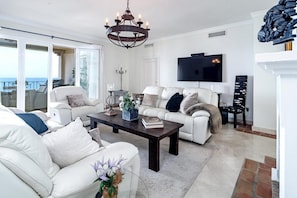 A spacious living room with a white sofa set, a dark wooden coffee table, and a large TV mounted on the wall. - Lap- 3 bed Apartment on the Beach. Families Only (Casares)