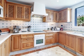 A kitchen with wooden cabinets, a white stove, and a window with a view of palm trees. - Lap- 3 bed Apartment on the Beach. Families Only (Casares)