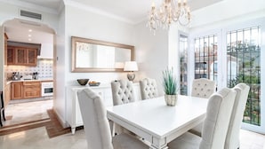 A dining area with a white table, cushioned chairs, a chandelier, and a view through large windows. - Lap- 3 bed Apartment on the Beach. Families Only (Casares)