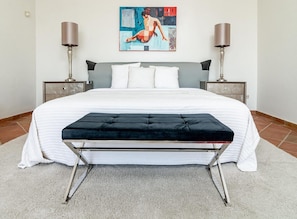 A neatly made bed with a black upholstered bench in front, two bedside lamps, and a painting on the wall. - Lap- 3 bed Apartment on the Beach. Families Only (Casares)