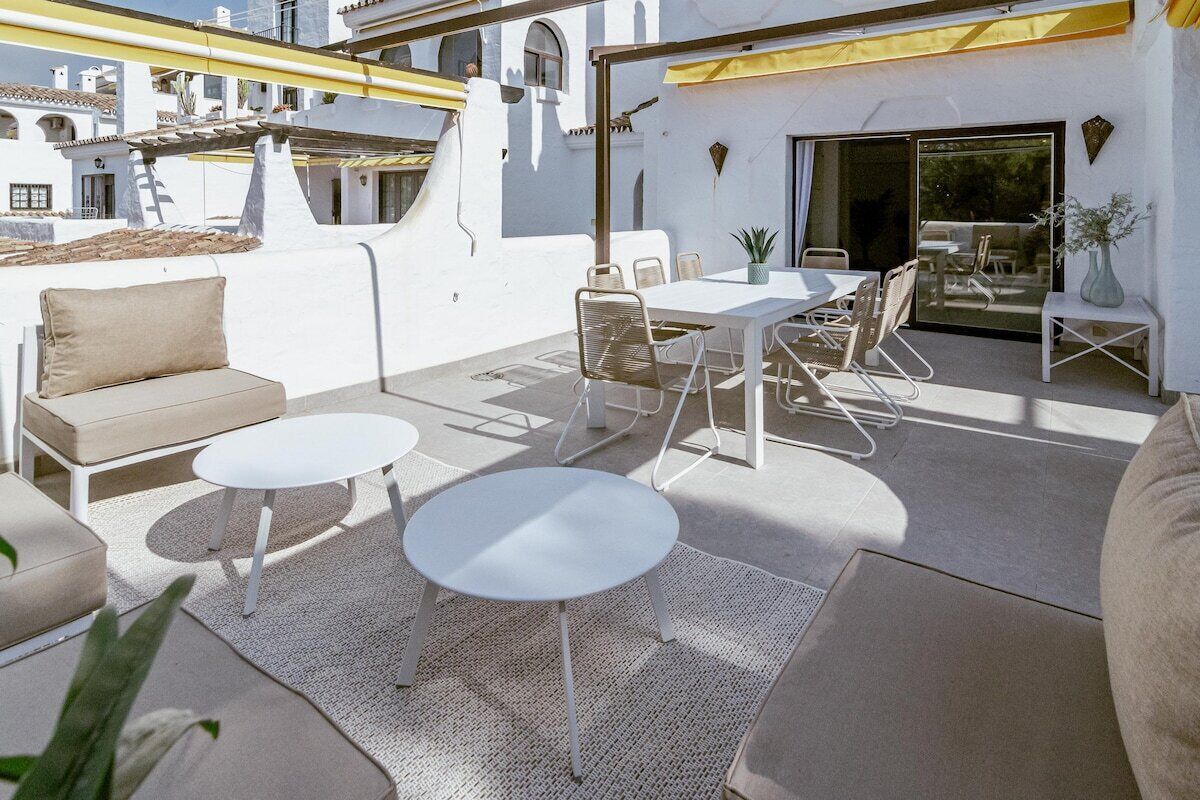 Um terraço no telhado com uma mesa e cadeiras brancas, um sofá e uma pequena mesa redonda.