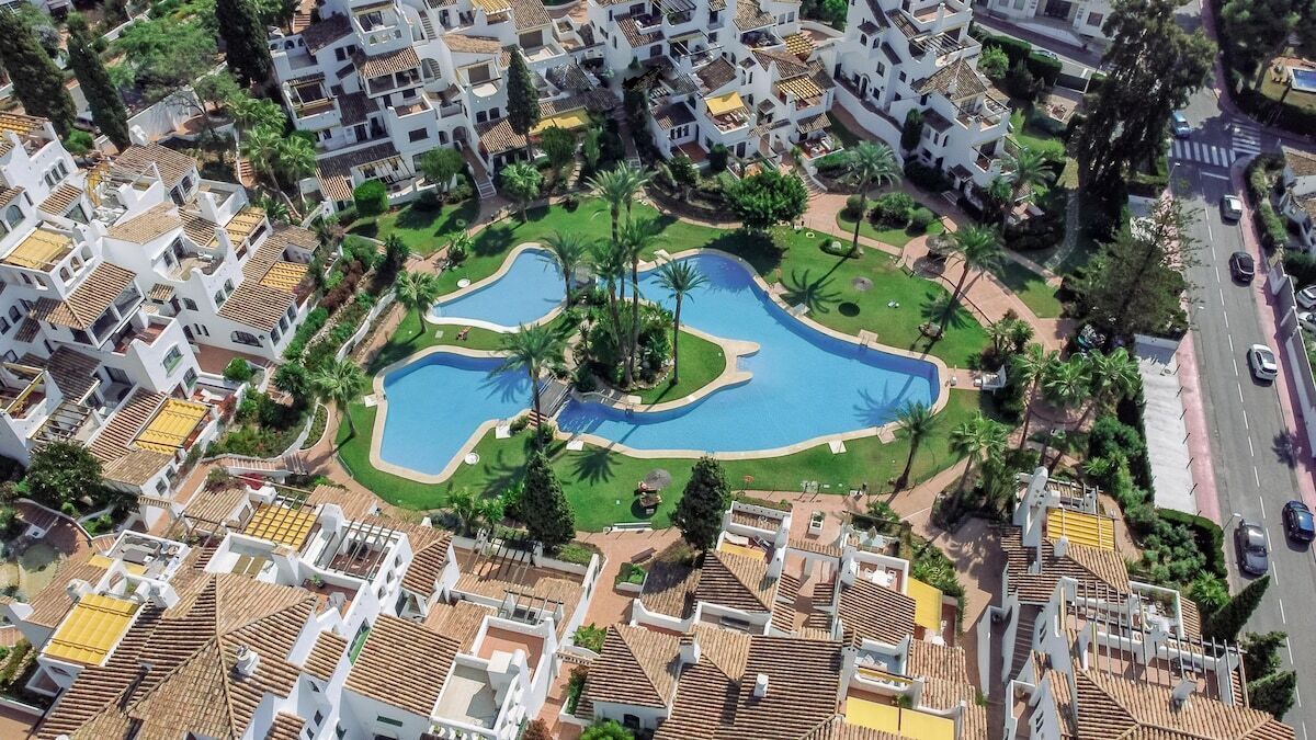 Zona residencial com piscina central rodeada por vegetação e edifícios brancos com telhados de terracota.