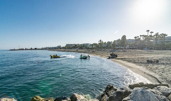 Une plage avec une eau d’un bleu limpide, un rivage rocheux et quelques bateaux.