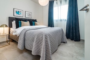 A modern bedroom with a large bed, a bedside table, and a wall-mounted lamp. - Inf4.5p- Modern 3 bed City Apartment Next to Beach (Estepona)