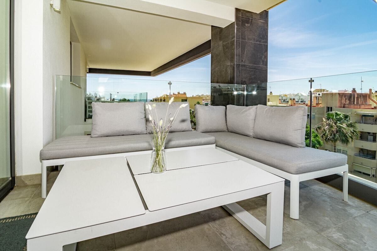 A modern living room with a sectional sofa, a white coffee table, and a view of the cityscape.