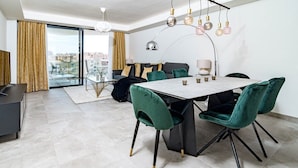 Un espace de restauration moderne avec une table en marbre, des chaises en velours vert et une vue sur la ville grâce à de grandes portes vitrées.