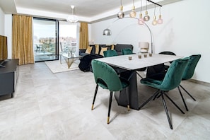 A modern dining area with a marble table, green velvet chairs, and a city view through large glass doors. - Inf4.5p- Modern 3 bed City Apartment Next to Beach (Estepona)