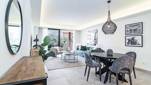 A modern living room with a dining area, featuring a round table, grey upholstered chairs, a sofa with a green cushion, and a large mirror on the wall. - Inf32l- Modern City Apartment, Families Only (Estepona)