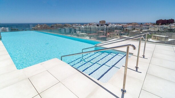 A rooftop swimming pool with clear blue water, surrounded by a white tiled deck and metal railings. - Inf32l- Modern City Apartment, Families Only (Estepona)