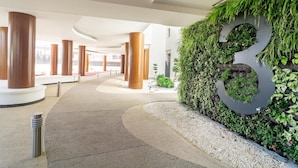 A modern hotel lobby with a curved pathway, large wooden columns, and a wall with a large number '8' covered in greenery. - Inf32l- Modern City Apartment, Families Only (Estepona)