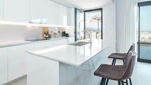 A modern kitchen with a large island, bar stools, and a view of the city through large windows. - Lme9f1- Penthouse, Amazing Views, Families Only (Estepona)