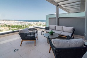 A balcony with a sofa, chairs, and a table, overlooking a cityscape and the sea. - Lme9f1- Penthouse, Amazing Views, Families Only (Estepona)