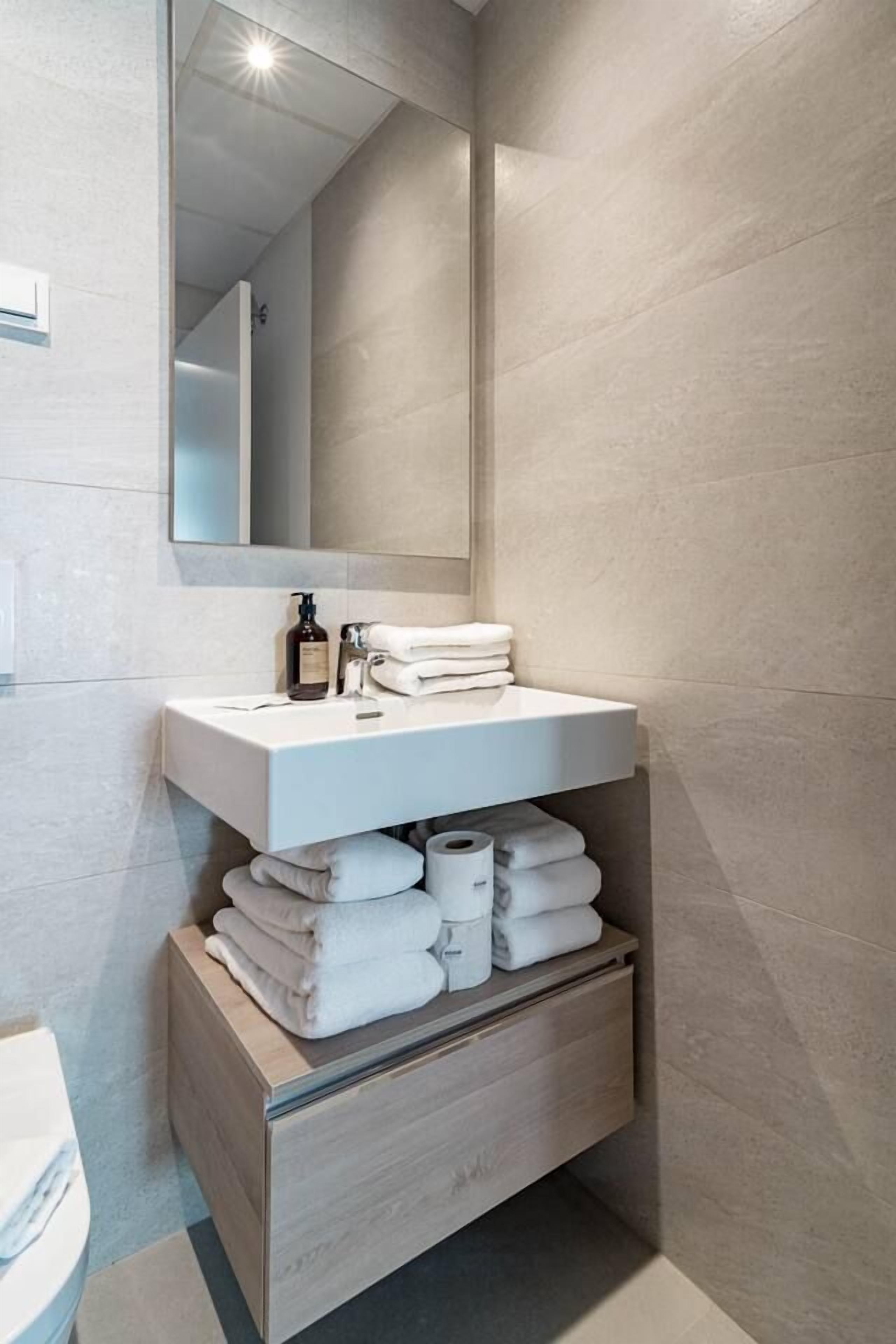 Un baño moderno con un lavabo blanco, un espejo y cajones para guardar objetos.