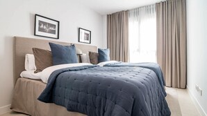 A double bed with a dark blue duvet and beige bedding, two framed pictures on the wall, and a window with beige curtains. - Lme9f1- Penthouse, Amazing Views, Families Only (Estepona)