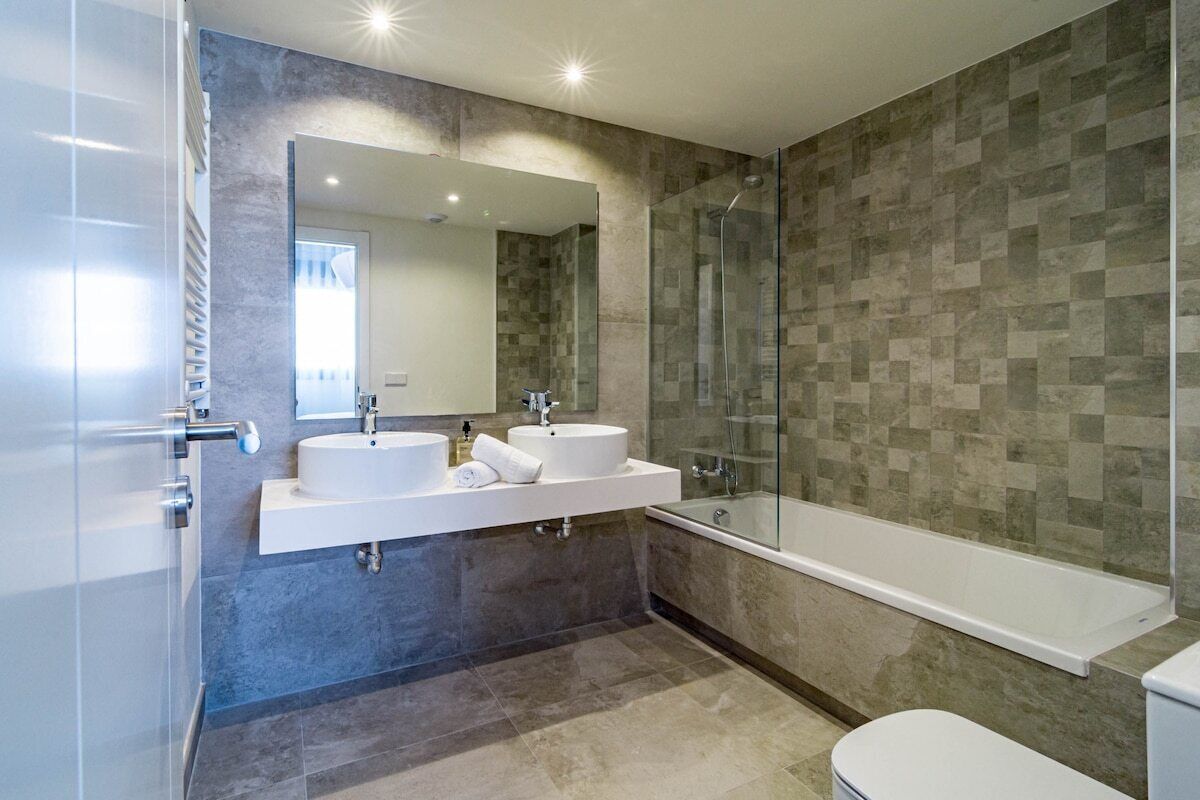 Ein modernes Badezimmer mit zwei Waschbecken, einer Duschkabine aus Glas und einer Badewanne.