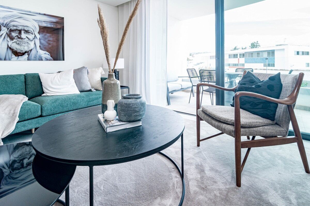 Una sala de estar moderna con un sofá verde, una mesa de centro redonda negra y una silla de mimbre.