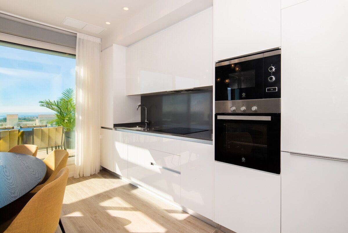 A modern kitchen with white cabinetry, a black stove, and a dining area with a table and chairs.
