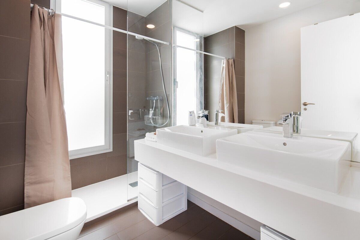 A modern bathroom with a glass shower enclosure, a double sink vanity, and a toilet.