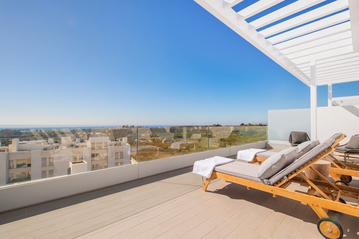 A rooftop terrace with two sun loungers, a glass balustrade, and a clear view of the cityscape.