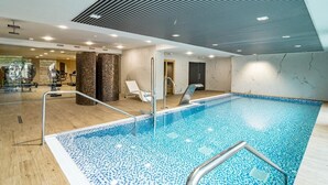 Una piscina interior con suelo de baldosas, una escalera de metal y un techo con diseño lineal.