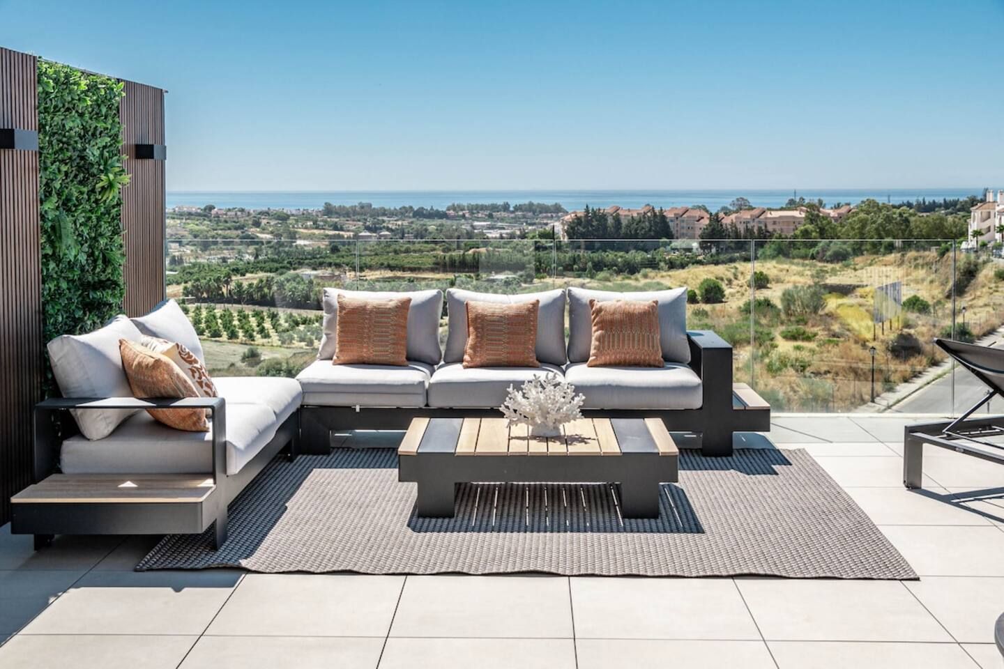 A modern outdoor seating area with a sofa and cushions, a coffee table, and a view of the landscape.