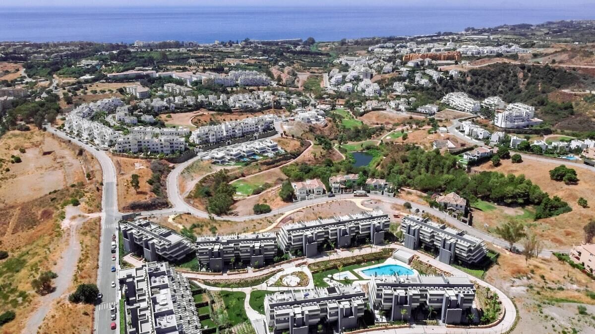 A residential area with modern apartment buildings, a central pool, and a road curving through the property.