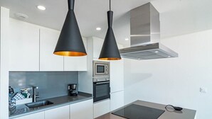 Una cocina moderna con armarios blancos, encimera negra y dos lámparas colgantes negras con tonalidades naranja.