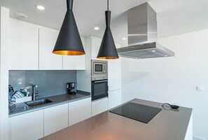 Una cocina moderna con armarios blancos, encimera negra y dos lámparas colgantes negras con tonalidades naranja.
