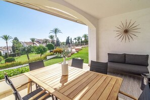 Une terrasse ensoleillée avec une table en bois, des chaises et un canapé. Un élément décoratif est visible sur le mur.