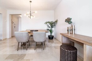 Un coin repas avec une table en bois, deux chaises, une plante en pot et un luminaire moderne.