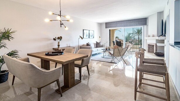Una sala de estar moderna con una mesa de comedor de madera, asientos cómodos, un ventanal con vistas y un televisor de pantalla plana montado en la pared.