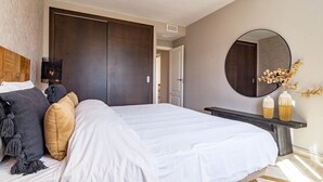 Un dormitorio con una cama grande, un armario de madera oscura, un espejo redondo y una pequeña mesa con objetos decorativos.
