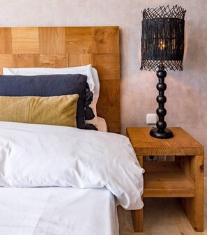 Un lit avec une literie blanche, une tête de lit en bois et une table de chevet sur laquelle se trouve une lampe noire.