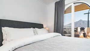 A hotel room with a bed, a view of the mountains, and a balcony with a chair and table. - Sam24i- Cozy Apartment Walking Distance to Beach (Marbella)