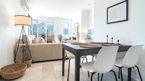 A modern living room with a dining area, featuring a sofa, dining table, and chairs. - Sam24i- Cozy Apartment Walking Distance to Beach (Marbella)