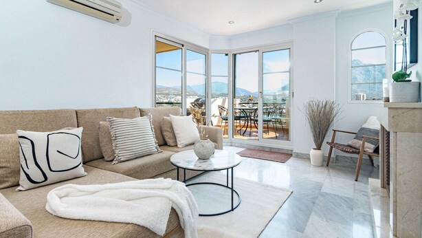 A spacious living room with a beige sofa, a round coffee table, and a view of a balcony with outdoor furniture. - Sam24i- Cozy Apartment Walking Distance to Beach (Marbella)
