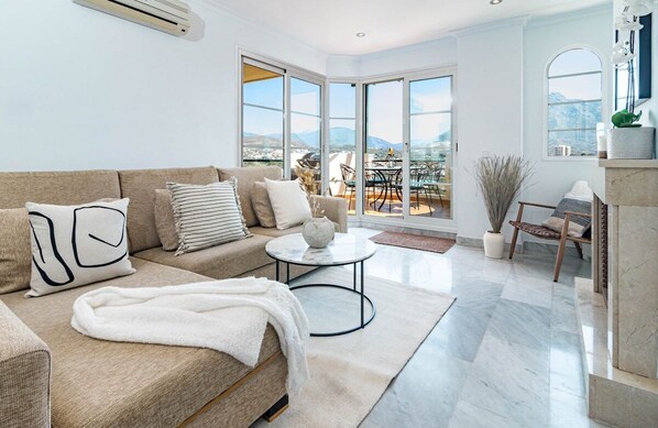 A spacious living room with a beige sofa, a round coffee table, and a view of a balcony with outdoor furniture. - Sam2.4i- Cozy Apartment Walking Distance to Beach (Marbella)