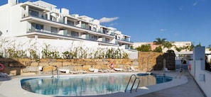 A modern hotel with a swimming pool, lounge chairs, and a stone wall. - Lm11.1a- Modern Flat, Amazing Views (Estepona)