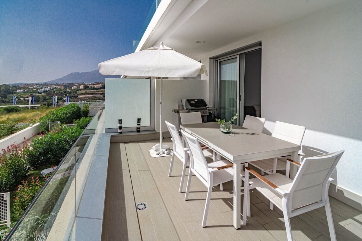 Un balcon avec une table et des chaises, un barbecue et une vue sur le paysage.