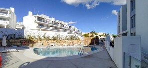 Una piscina con sillones de descanso y un muro de piedra, rodeada de edificios modernos.
