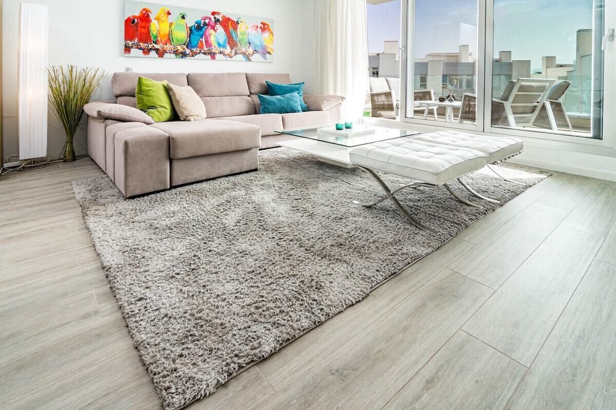 Un soggiorno moderno con un divano beige, un tavolino in vetro e un'ampia finestra con vista sulla città.