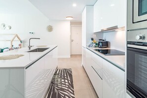 A modern kitchen with white cabinetry, a built-in oven, and a coffee machine. - Lme2ba- Cozy Ground Floor Flat in Luxury Resort (Estepona)