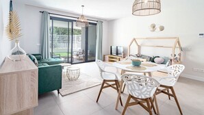 A modern living room with a green sofa, white chairs, a round table, and a wooden playhouse. - Lme2ba- Cozy Ground Floor Flat in Luxury Resort (Estepona)