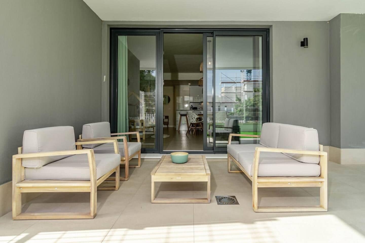 A modern outdoor seating area with two sofas and a coffee table, a sliding glass door leading to an interior space, and a small outdoor light fixture.