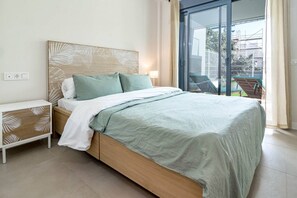 A bedroom with a bed, nightstands, a wooden headboard, and a view of the outside. - Lme2ba- Cozy Ground Floor Flat in Luxury Resort (Estepona)