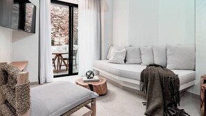 Una sala de estar moderna con un sofá, una silla de mimbre, una mesa redonda de madera y un televisor montado en la pared.