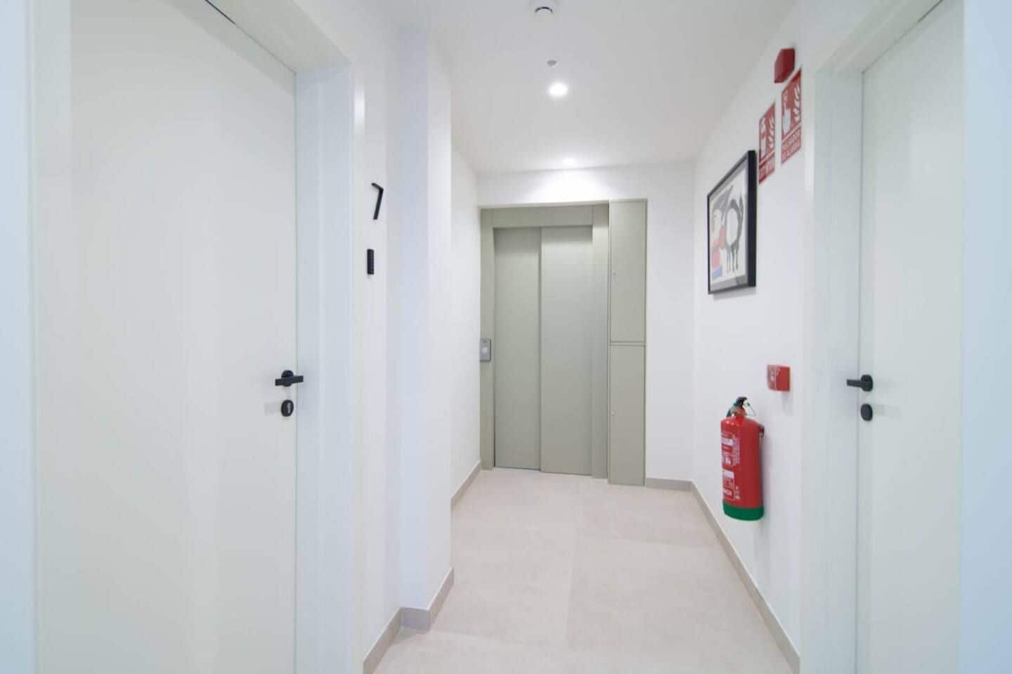 Un pasillo con puertas, un extintor y un cuadro en la pared.