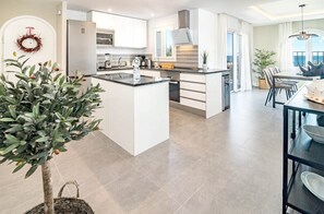 A modern kitchen with white cabinetry, a central island, and a dining area with a view. - Rdm9- Modern Family Apartment in Riviera del Mar (Mijas)