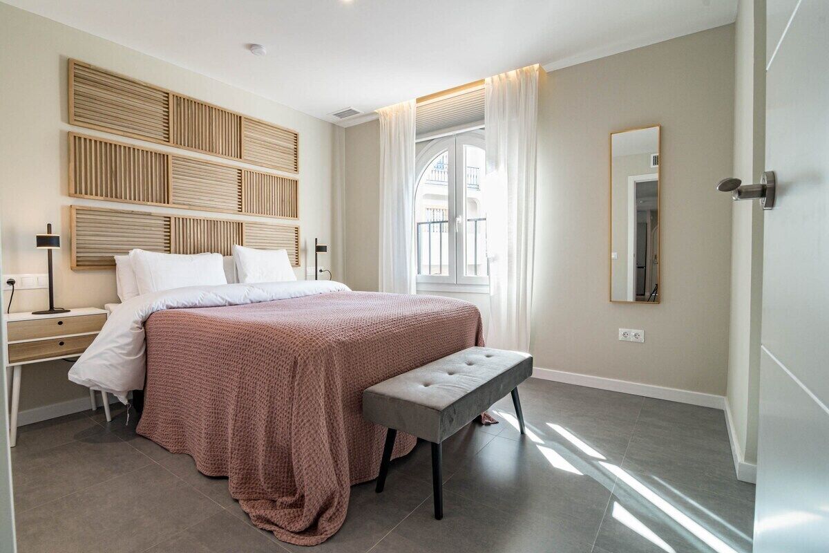 A modern bedroom with a large bed, a bench, a bedside table, and a wall-mounted headboard.