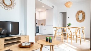 A modern living room with a flat-screen TV, wooden furniture, and a dining area with a round table and chairs. - GO- Golden Banus by Roomservices (Marbella)